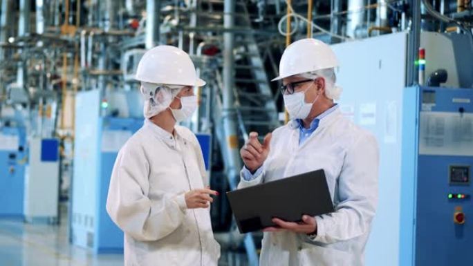 两个穿着实验室外套的工厂工人正在谈话。工程师，团队合作，现代化工厂设施。