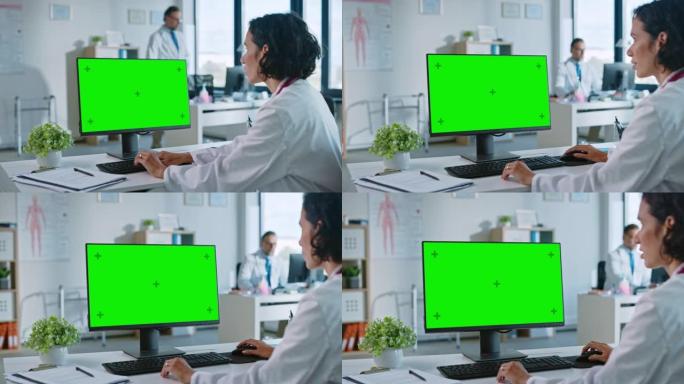 女医生正在健康诊所的绿屏模拟显示计算机上工作。穿着白大褂的助理正在医院办公室的桌子后面阅读病史。