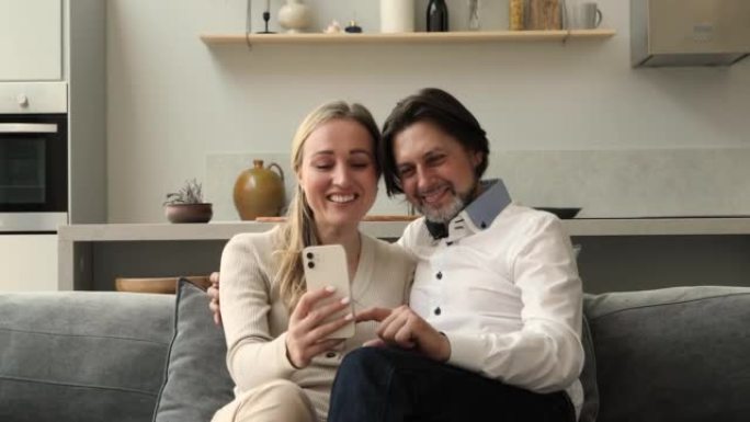 已婚夫妇在家拥抱沙发上放松使用智能手机