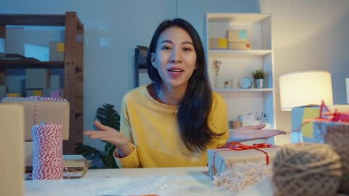 看着相机销售的快乐年轻亚洲女商人晚上在网上商店市场向客户视频直播介绍产品。