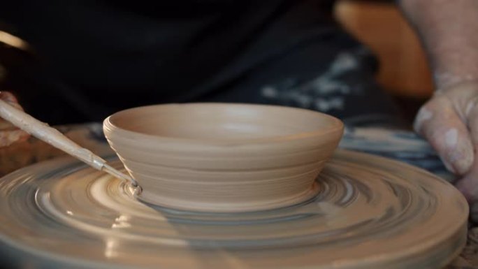 熟练的陶工在投掷轮上装饰漂亮的手工碗的特写镜头