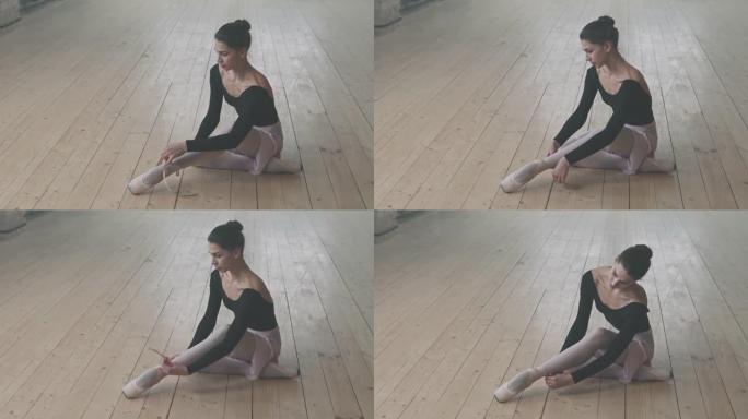 漂亮的芭蕾舞女演员在地板上系鞋带