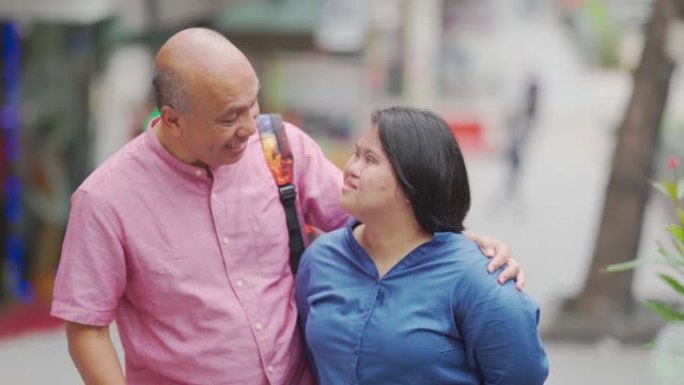 亚洲马来人退休父亲和他的唐氏综合症女儿在周末的结合时间在城市街道上聊天