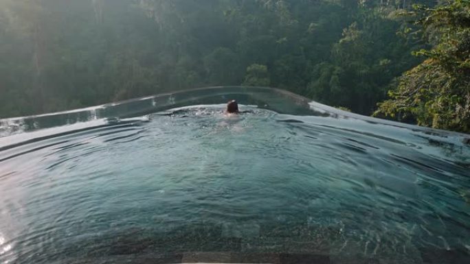 性感的女人在无边泳池游泳，享受异国情调的暑假在酒店水疗中心享受奢华的生活方式，可以看到热带丛林