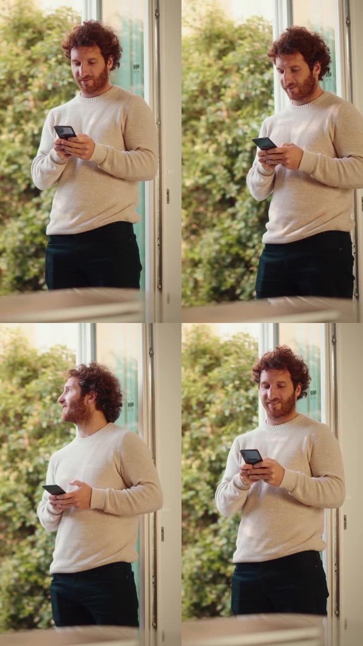 垂直屏幕: 英俊的成年男子，姜黄色卷发使用智能手机，站在家里的客厅。男性喜欢喝一杯浓缩咖啡，查看社交