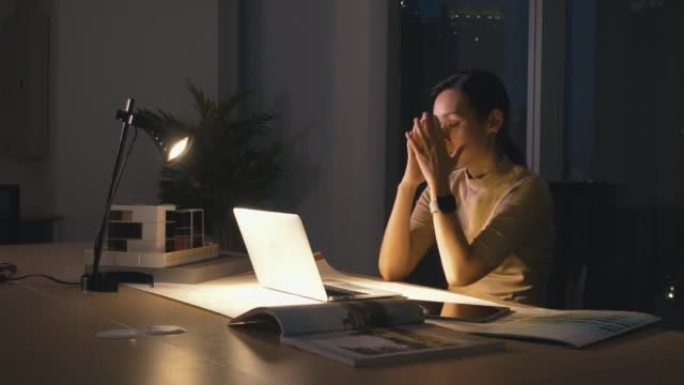 昏昏欲睡的女商人晚上坐在办公室时在笔记本电脑上工作