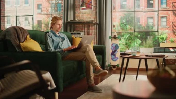 年轻英俊的成年男子坐在阁楼客厅的沙发上，在家用笔记本电脑工作。创意男性查看社交媒体，浏览互联网。从大