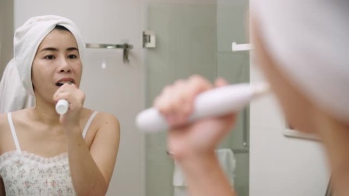 亚洲妇女在浴室用汽车牙刷装置刷牙