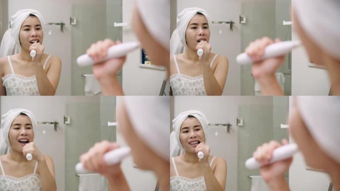 亚洲妇女在浴室用汽车牙刷装置刷牙