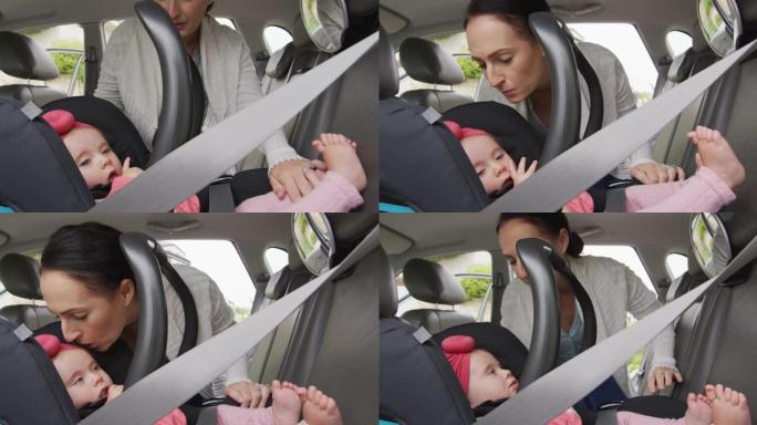 高加索母亲在汽车的安全座椅上亲吻婴儿