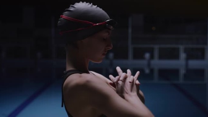 年轻的职业女游泳者戴着帽子和护目镜的电影镜头正在进行热身运动，同时准备在游泳池训练。运动、竞争、胜利