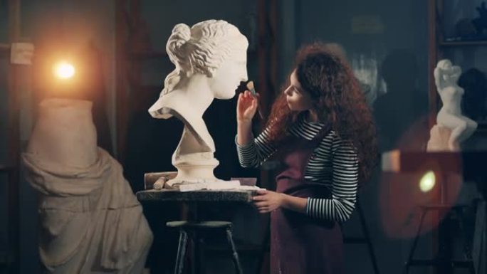 Lady artist在刷完石膏雕塑后正在看。艺术概念，创意工作室室内。