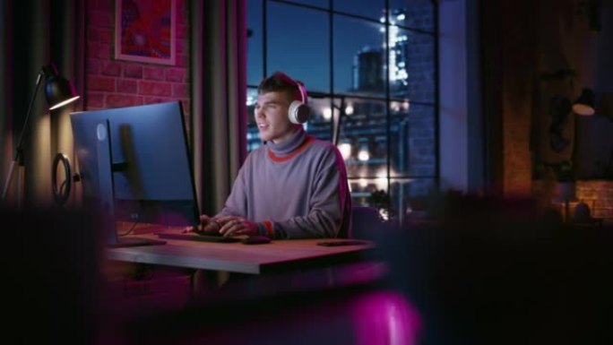 晚上，戴着耳机的年轻帅哥在时尚的阁楼公寓里使用电脑。富有创造力的男性微笑，在家工作，在社交媒体上浏览