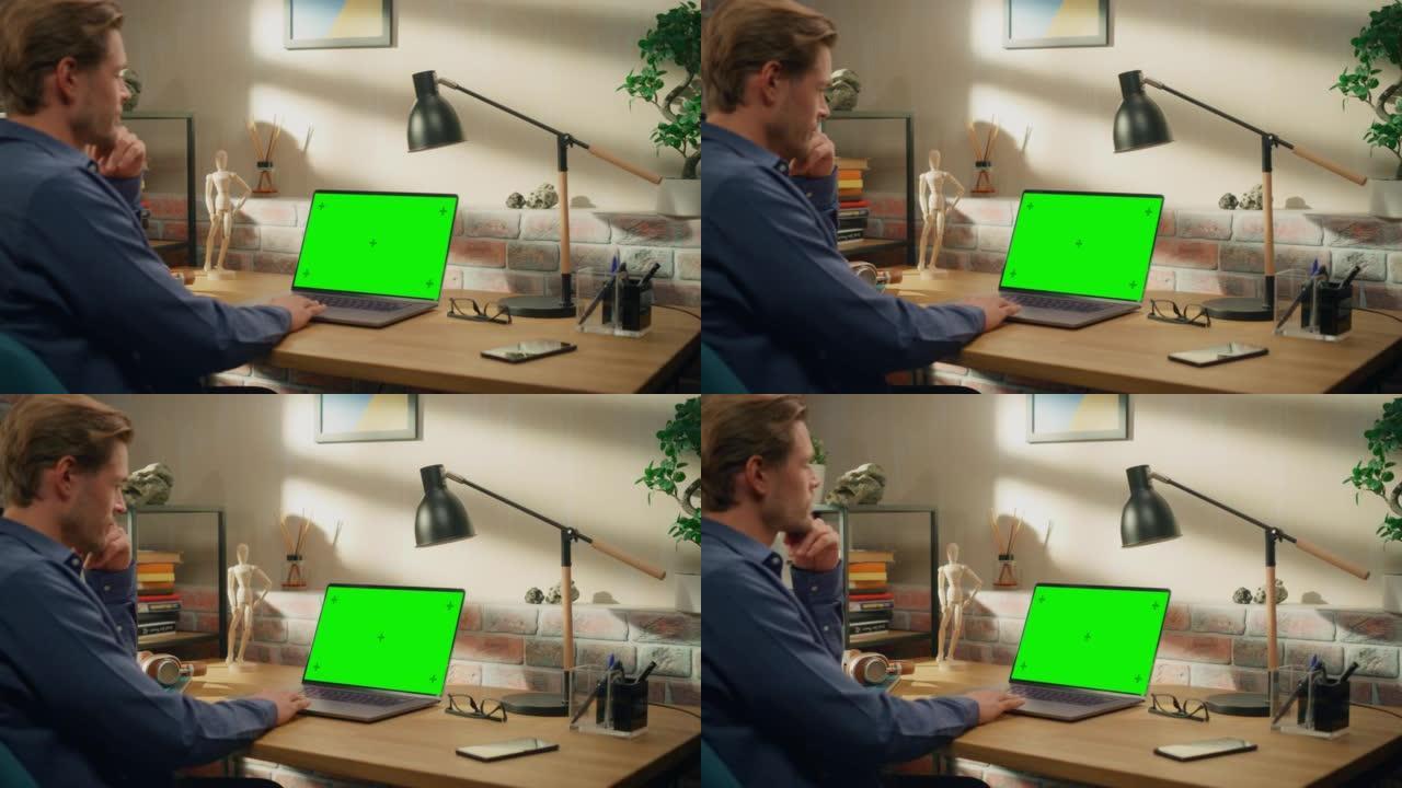 年轻英俊的男人在家工作，手提电脑上有绿屏模拟显示。创意男性查看社交媒体，浏览互联网。阁楼城市公寓的客
