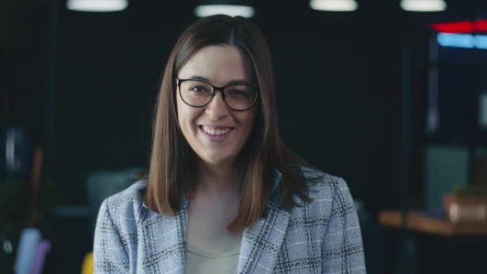 幸福美丽的老板商务女性戴眼镜，正装在模糊的工作场所背景对着镜头微笑。