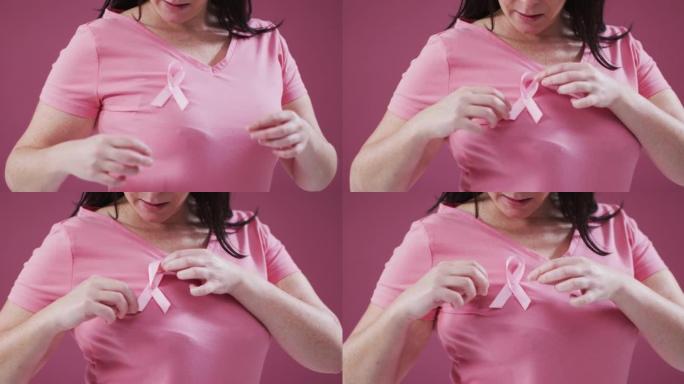 一个女人的中间部分在粉红色的背景下触摸她胸前的粉红色丝带