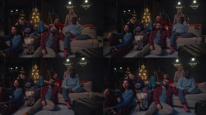 一群快乐的年轻多元化的朋友在圣诞之家庆祝派对慢动作时，在舒适的沙发上的电视上看电影。