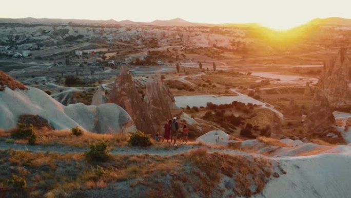 无人机与孩子们一起在卡帕多西亚的山岩顶上观看史诗般的日出风景全景，在快乐的家庭中飞翔。