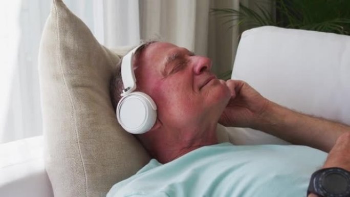 白人老人躺在家里的沙发上戴着耳机唱歌