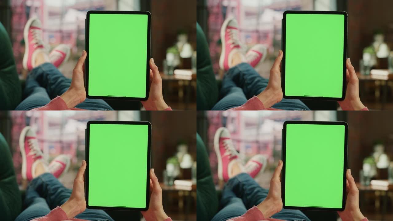 带有绿屏模拟显示的平板电脑上的女性手滚动饲料。女性在家里的沙发上放松，在移动设备上观看视频和阅读社交