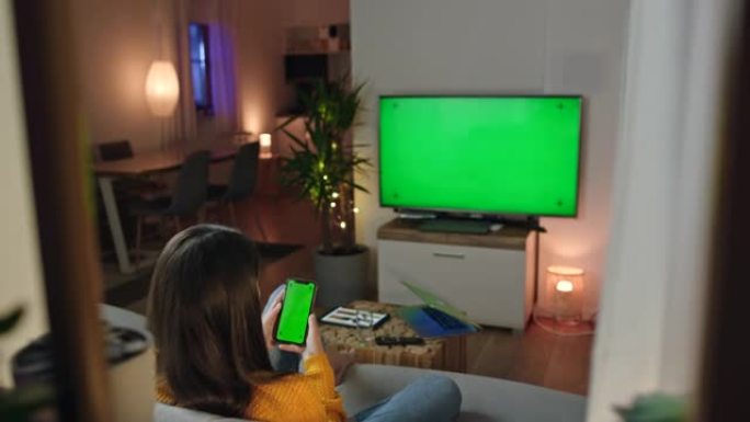 DS年轻女子使用智能手机和带色键绿屏的电视