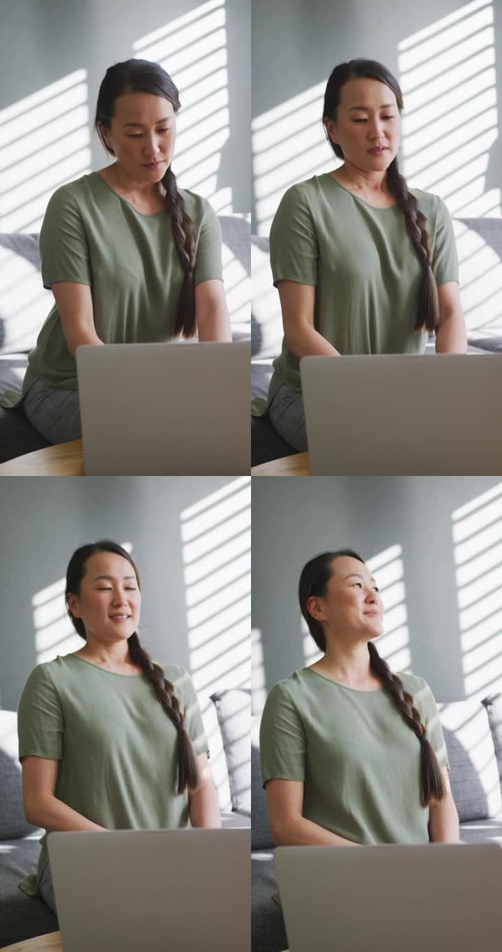 一名亚洲女子用笔记本电脑对着窗外微笑的垂直镜头
