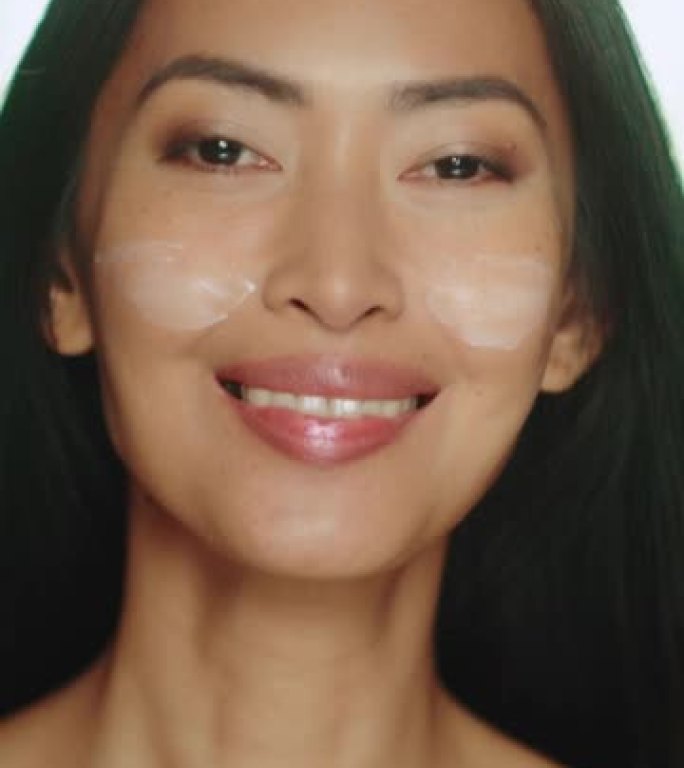 垂直屏幕。美丽的亚洲女人戏剧性地转身，用充满活力的手势涂抹面霜。女性用天然化妆品护肤品使皮肤柔软。绿