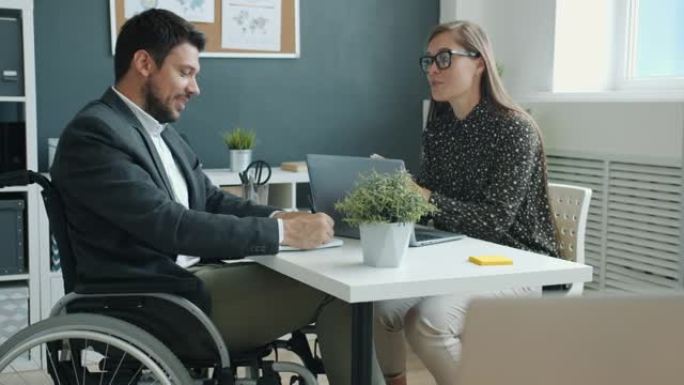 坐在轮椅上的残疾人与坐在办公室办公桌上的女同事讨论业务