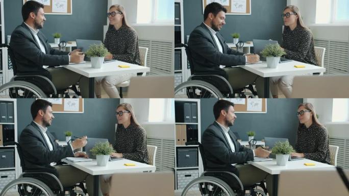 坐在轮椅上的残疾人与坐在办公室办公桌上的女同事讨论业务