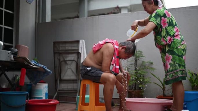 亚洲华裔高级妇女清洗丈夫的头发，在没有水的情况下在房子的前院洗头发