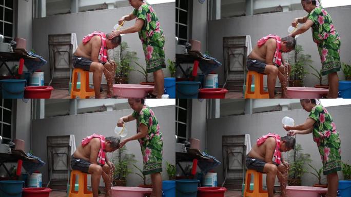 亚洲华裔高级妇女清洗丈夫的头发，在没有水的情况下在房子的前院洗头发