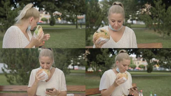 带防护口罩的SLO MO女人在公园吃汉堡并检查电话