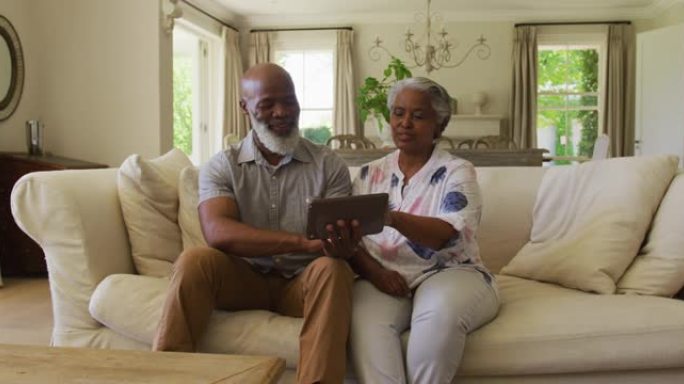 非裔美国老年夫妇在家里使用数字平板电脑时互相看着对方微笑