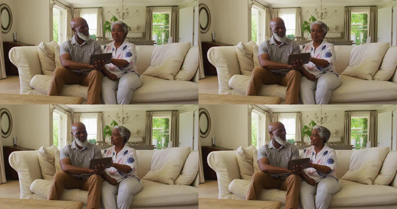 非裔美国老年夫妇在家里使用数字平板电脑时互相看着对方微笑