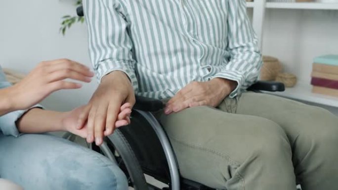 轮椅上的残障男子握着女人的手表达爱与支持的特写