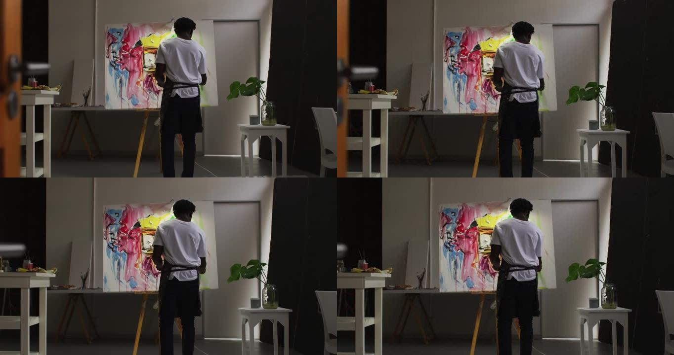 非裔美国男性艺术家在艺术工作室的画布上穿着围裙绘画的后视图
