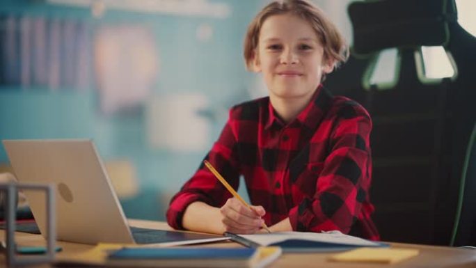 一个聪明的小男孩在家里舒适的房间里的笔记本电脑上做作业的肖像。少年快乐，看着镜头微笑。家庭教育理念。