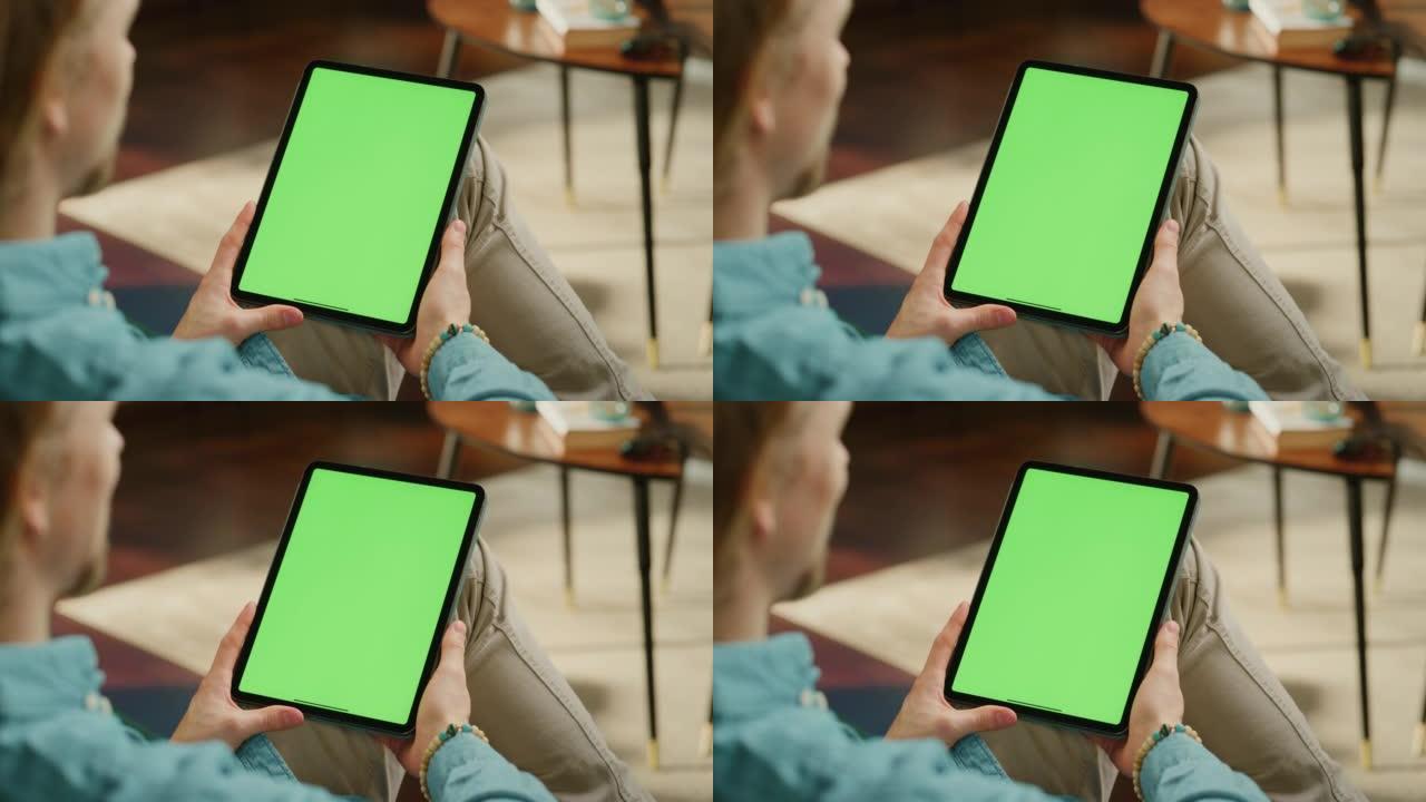 年轻人拿着平板电脑，绿屏模拟显示。男性在家放松，在移动设备上观看视频和阅读社交媒体帖子。特写肩膀上的