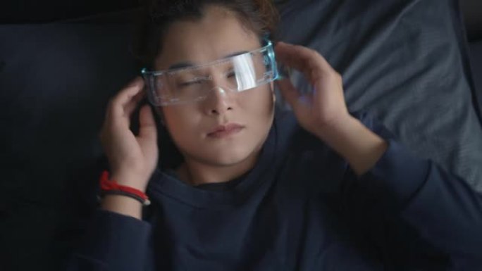 亚洲女性使用虚拟现实眼镜躺在床上，赛博朋克眼镜