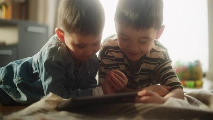 两个亚洲男性孩子的肖像在周末在他们的房间里使用数字平板电脑。两个可爱的兄弟姐妹看着他们最喜欢的孩子表