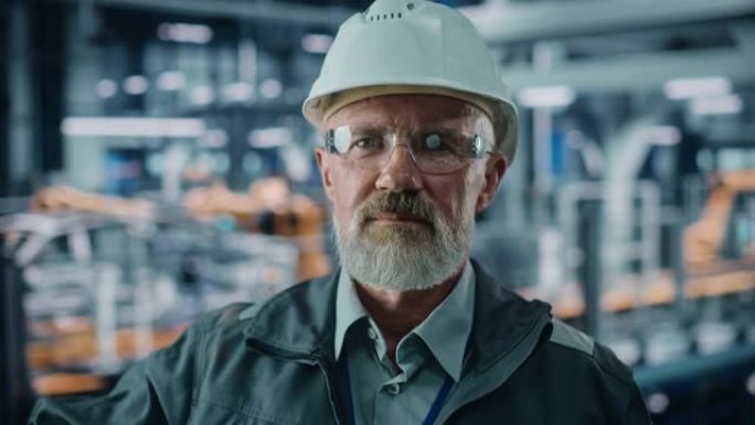 汽车厂办公室: 戴着安全安全帽的高级白人男性工程师的肖像，看着相机，微笑着。自动化机械臂装配线制造工