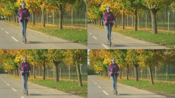 老年妇女在秋天绿树成荫的大道上骑电动踏板车