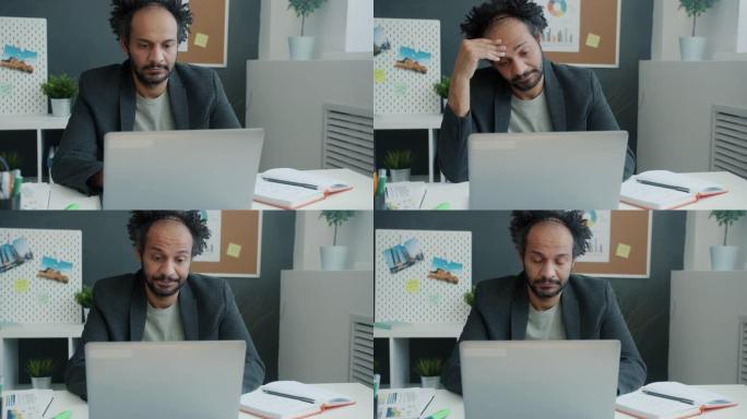 不快乐的员工用笔记本电脑触摸头部的慢动作肖像感到无聊和疲倦