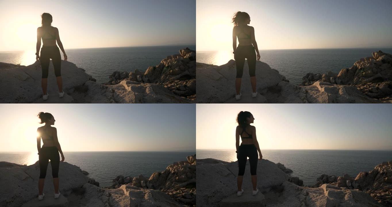 一位年轻的运动运动运动员在日落时在带有海景的岩石顶上进行跑步和慢跑锻炼后，正在欣赏全景。
