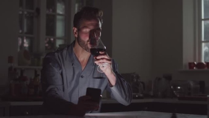 穿着睡衣的成熟男人晚上用手机坐在厨房喝杯酒