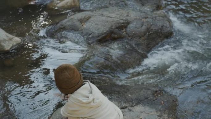 小男孩站在岩石上看着河