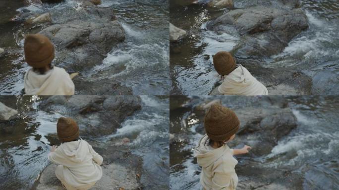 小男孩站在岩石上看着河