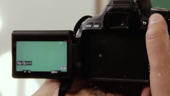 男子在学校教室里拿着绿屏背景的DSLR相机。特写。