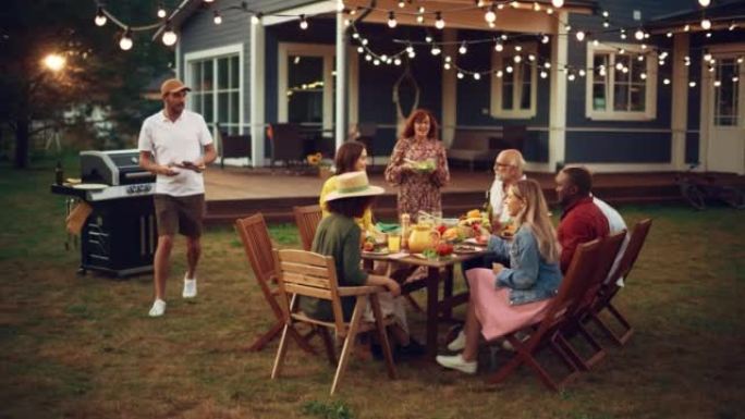 一群多民族的人在户外晚餐时玩得开心，互相交流，吃烧烤。在温暖的夏日下午，家人和朋友聚集在他们的家门外