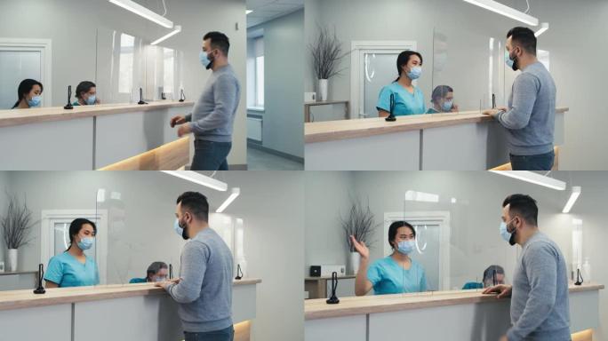 戴着面具的男子在医院接待时与护士交谈